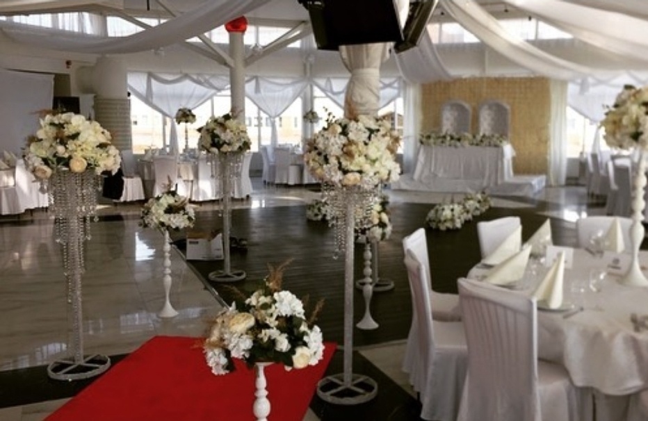 Höga blomsterpelare i vitt och crème med eleganta kristalldetaljer. Mjukt draperade tak, stilrena stolsuppsättningar och en vackert dekorerad fond